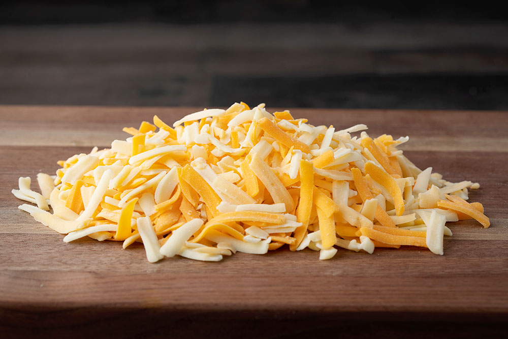 A pile of cheese on top of a wooden cutting board.